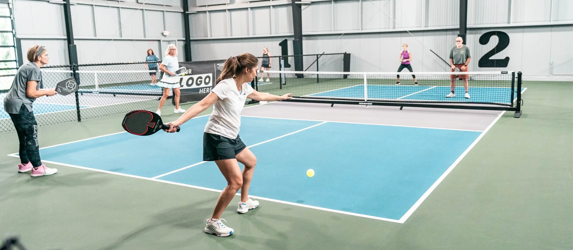 A woman serves a pickleball at an indoor pickleball court against another duos team.